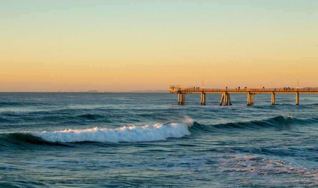 Captivating sunset at Gold Coast's pier with waves crashing beneath a golden sky.